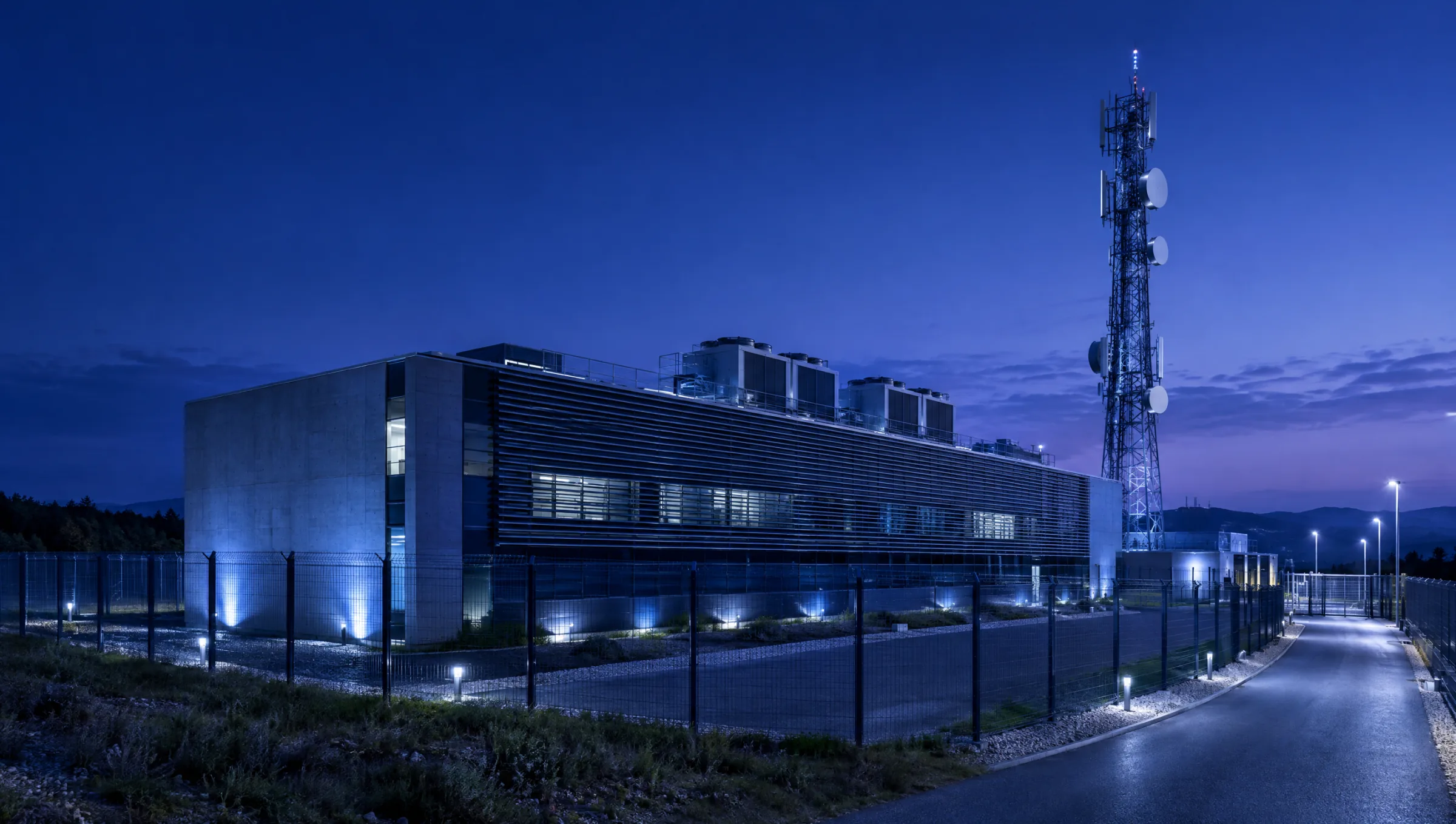 A telecom gateway building at dusk beside a communications tower